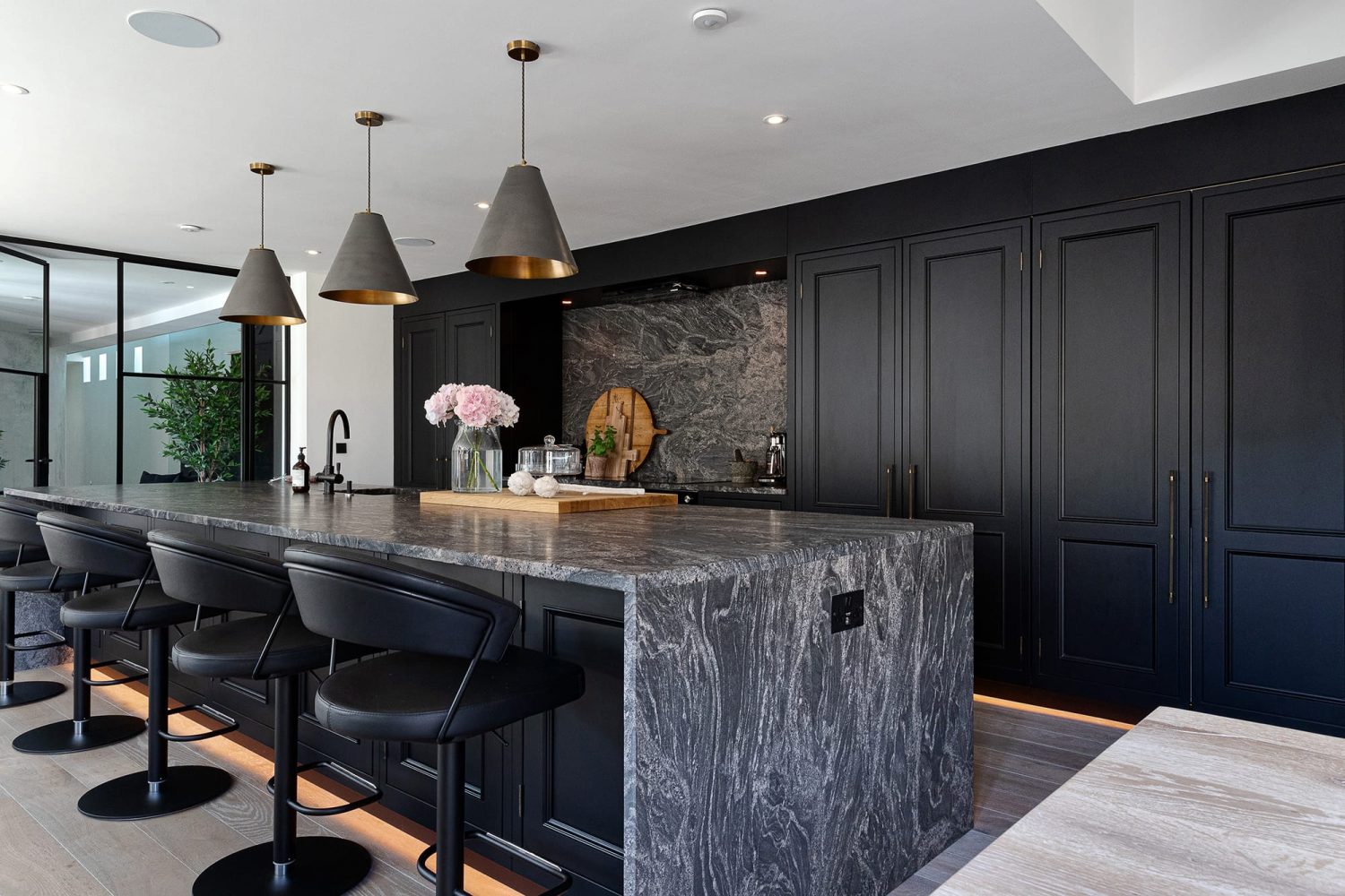 Kitchen with black cabinets and large island with dark marble countertop and black leather barstools
