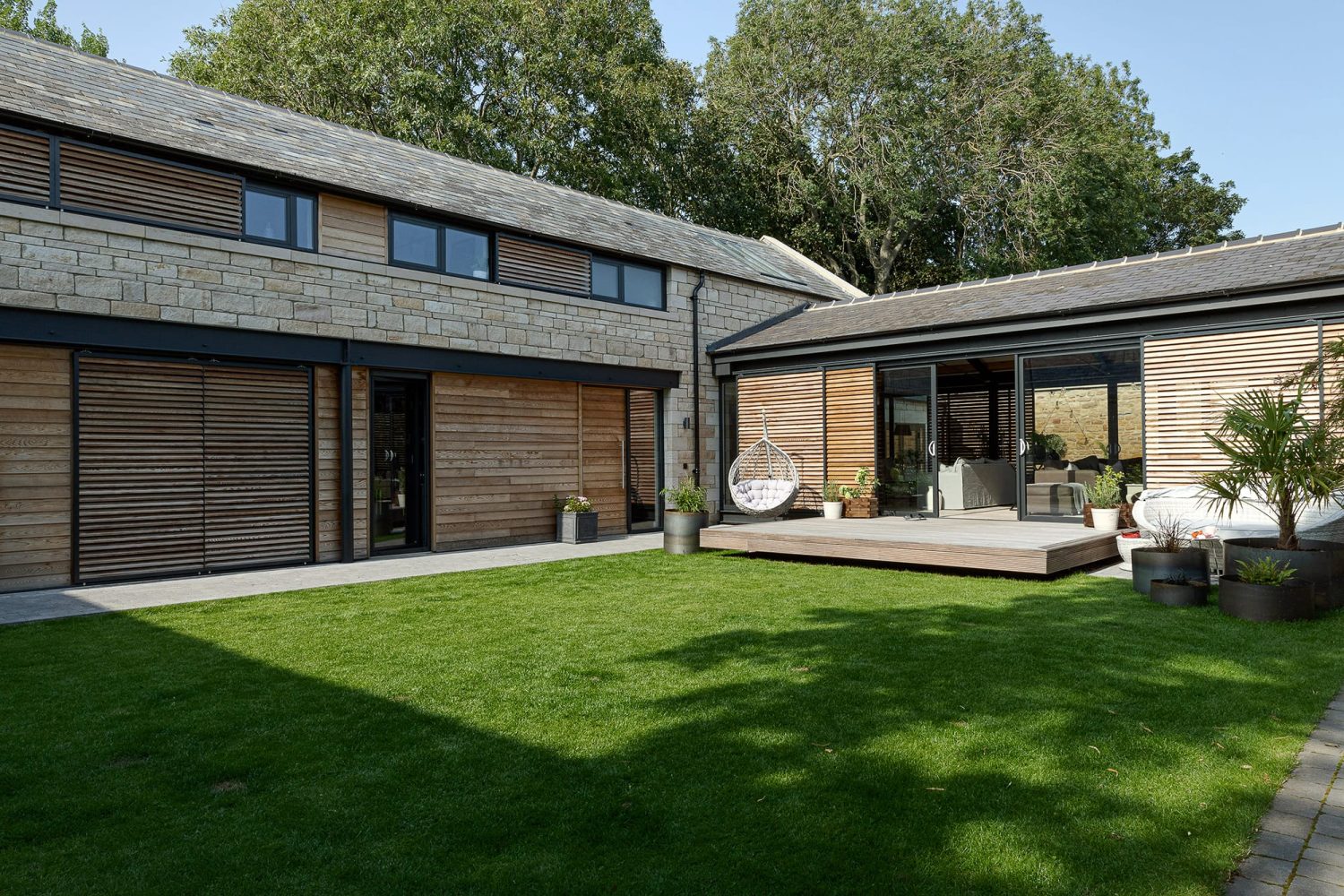 Garden of stone barn conversion with grass and decking area with plants around