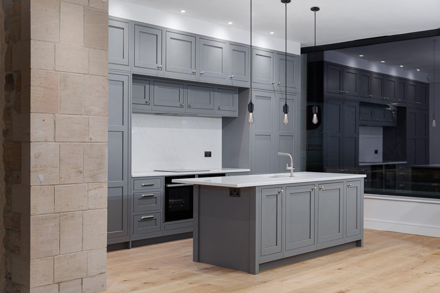 Kitchen with grey cabinets and island in the centre with white marble countertops and backsplash and three pendant lights hanging from the ceiling