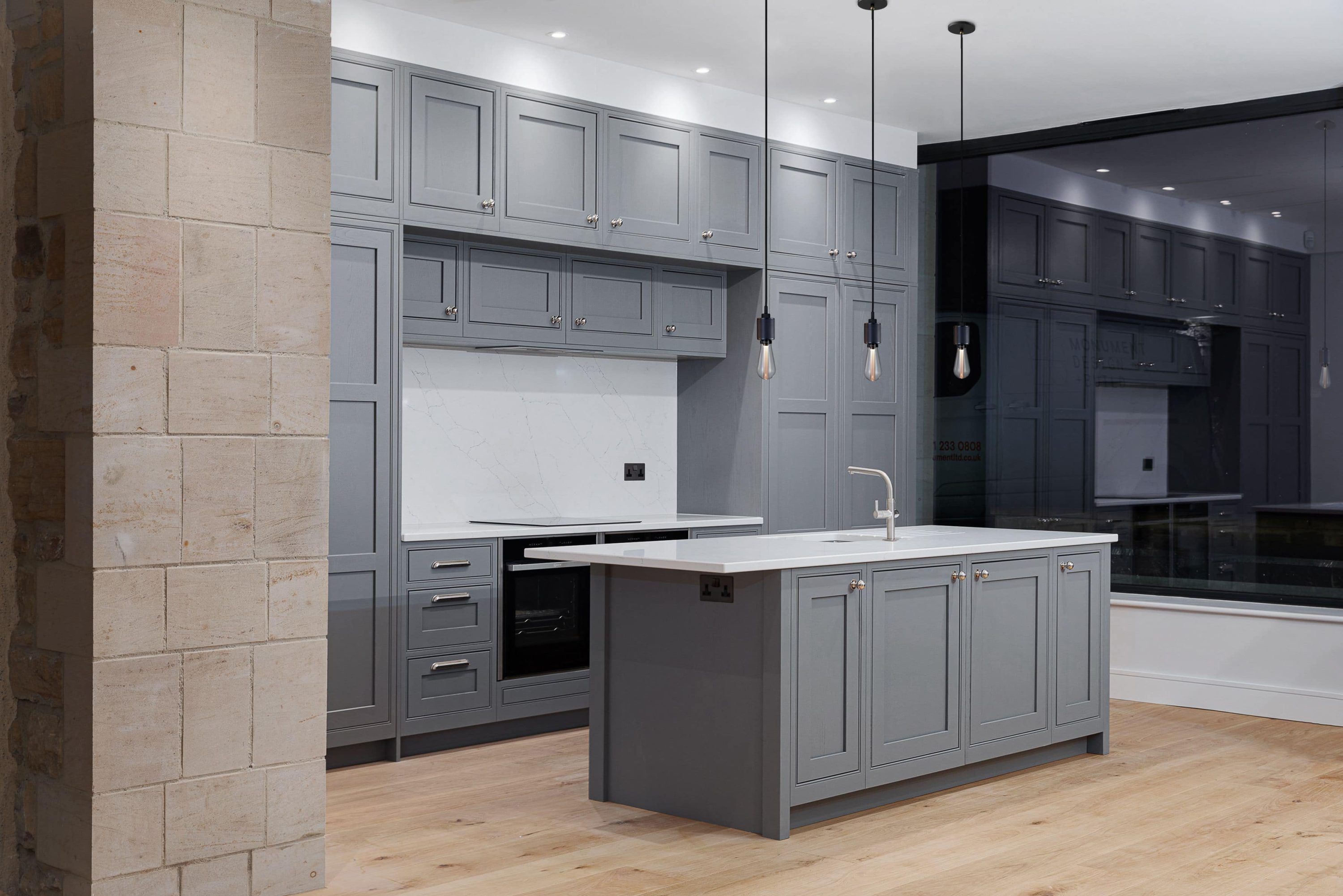 Kitchen with grey cabinets and island in the centre with white marble countertops and backsplash and three pendant lights hanging from the ceiling