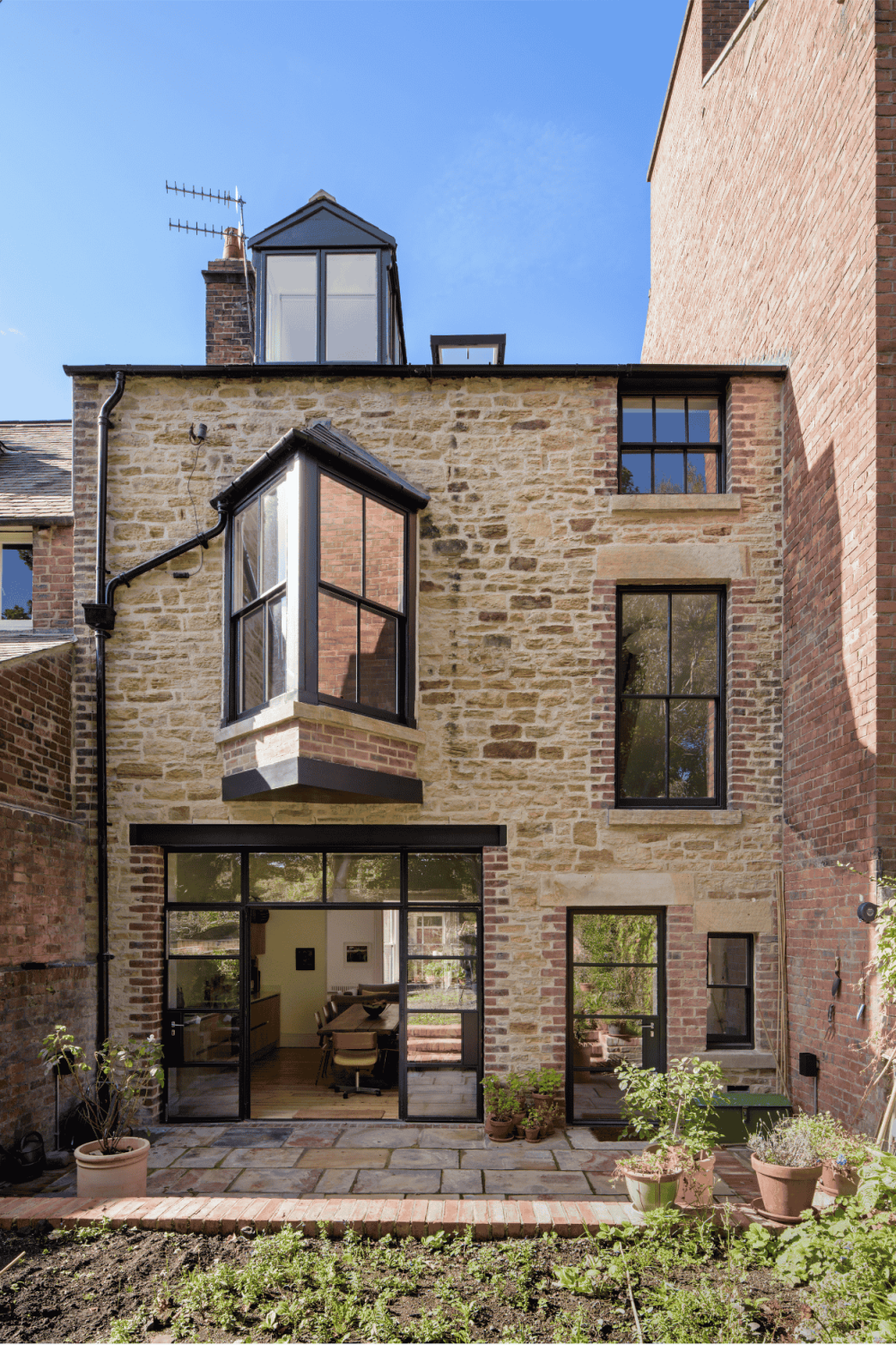 Exterior back of house with exposed brick and stone walls. Crittall style windows and doors and a planting bed outside.