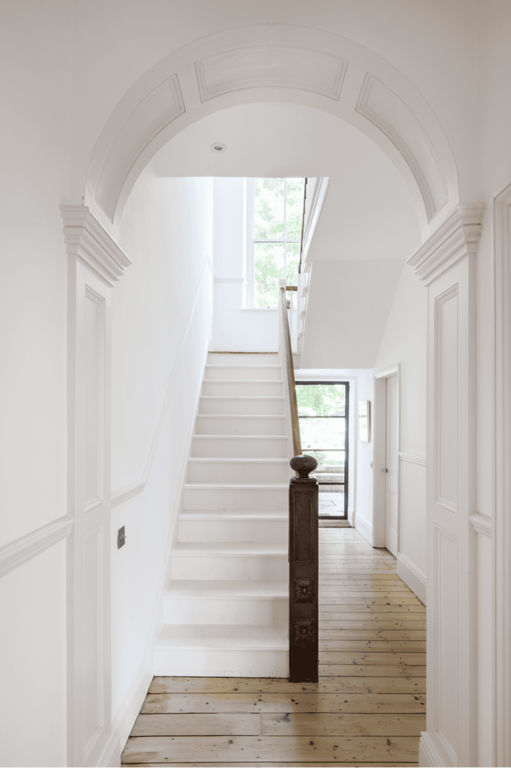Hallways with white walls and an archway leading through to white staircase with wooden banister