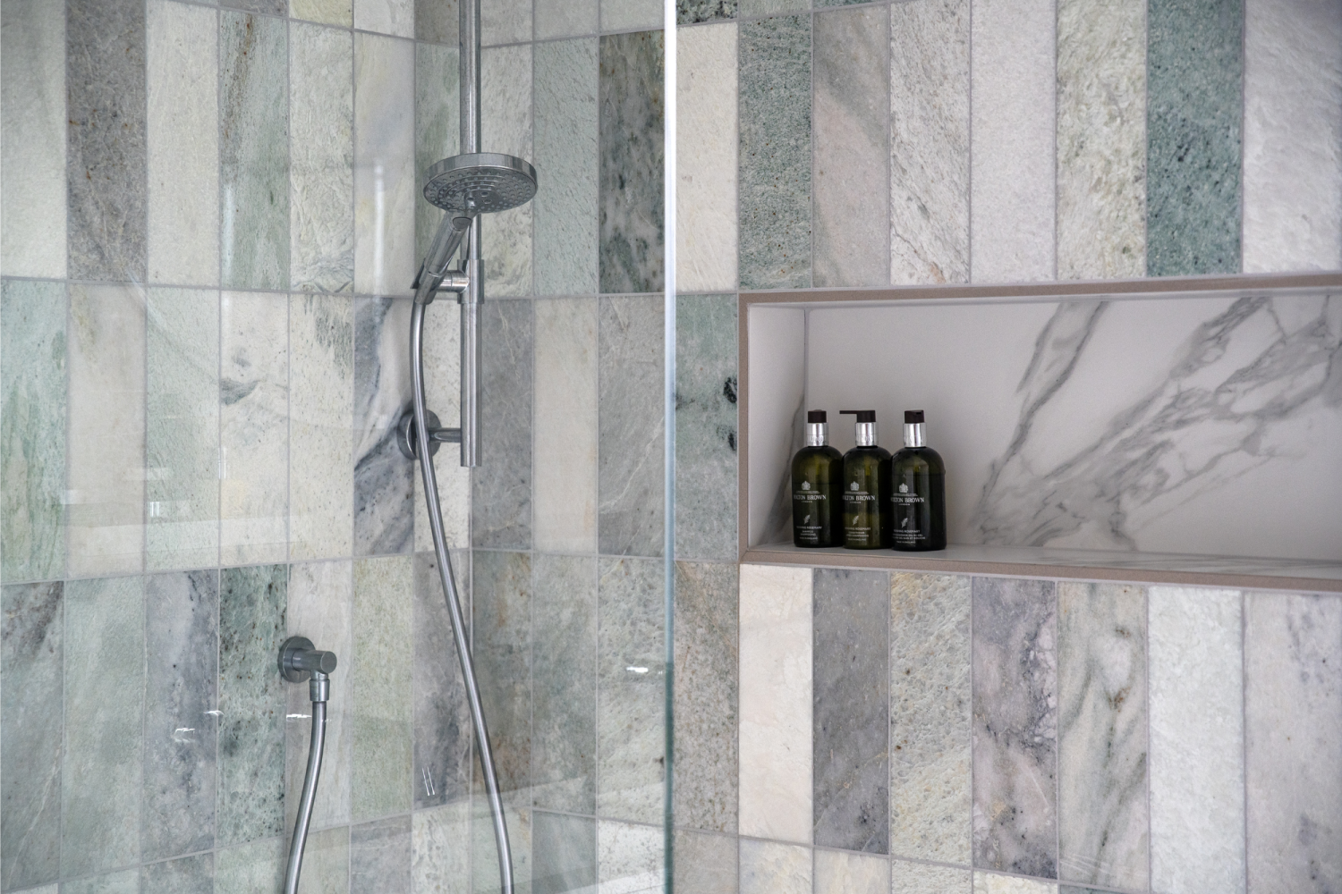 Shower with green and grey tiled walls, silver hardware and a shower niche holding bottles