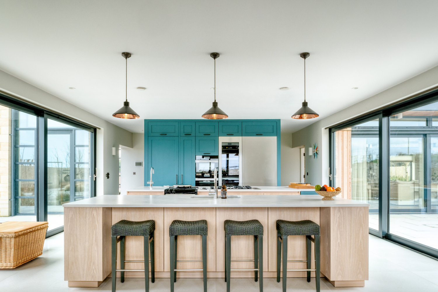 Kitchen with two islands in front of blue cabinets with black and copper lamps hanging from above