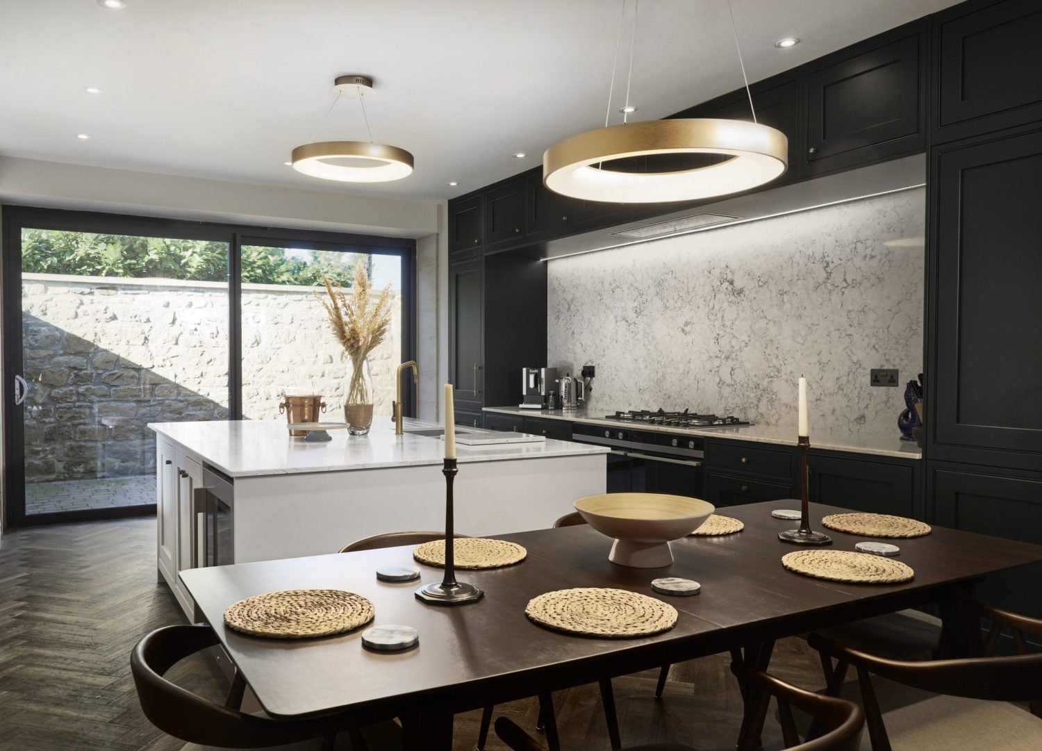 Kitchen with dark wooden dining table and white island with golden circular pendant lights hanging above