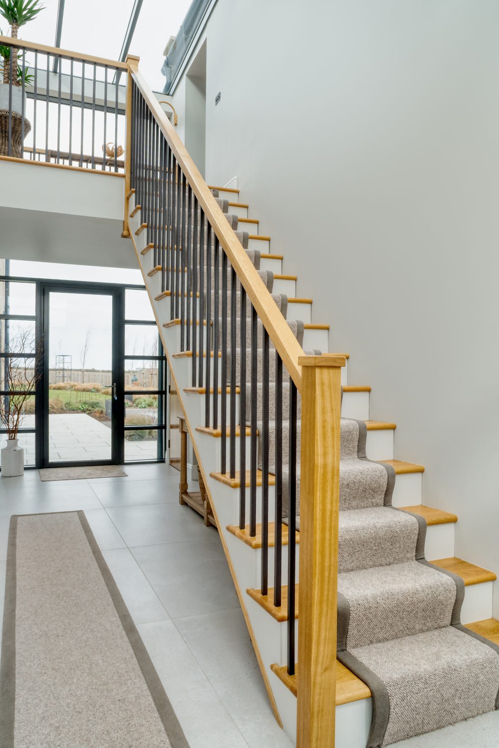 Hallway with white and wooden staircase to the right and glazed door behind leading outdoors