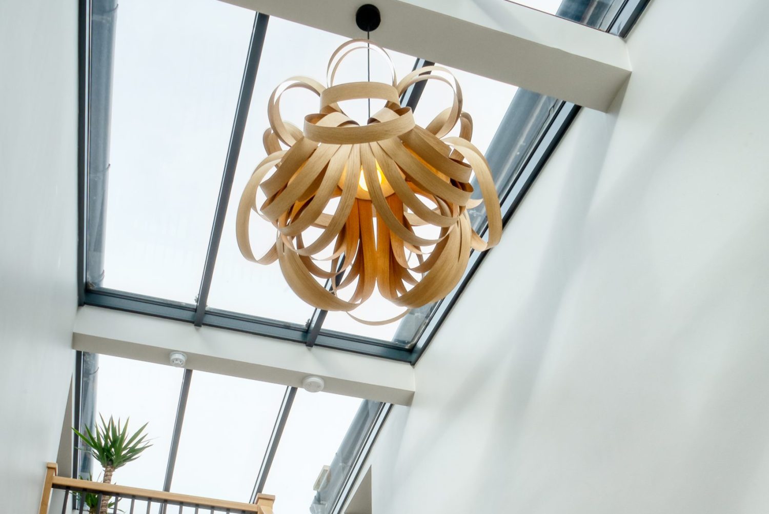 White and wooden staircase with large windows in ceiling above with large pendant lamp hanging