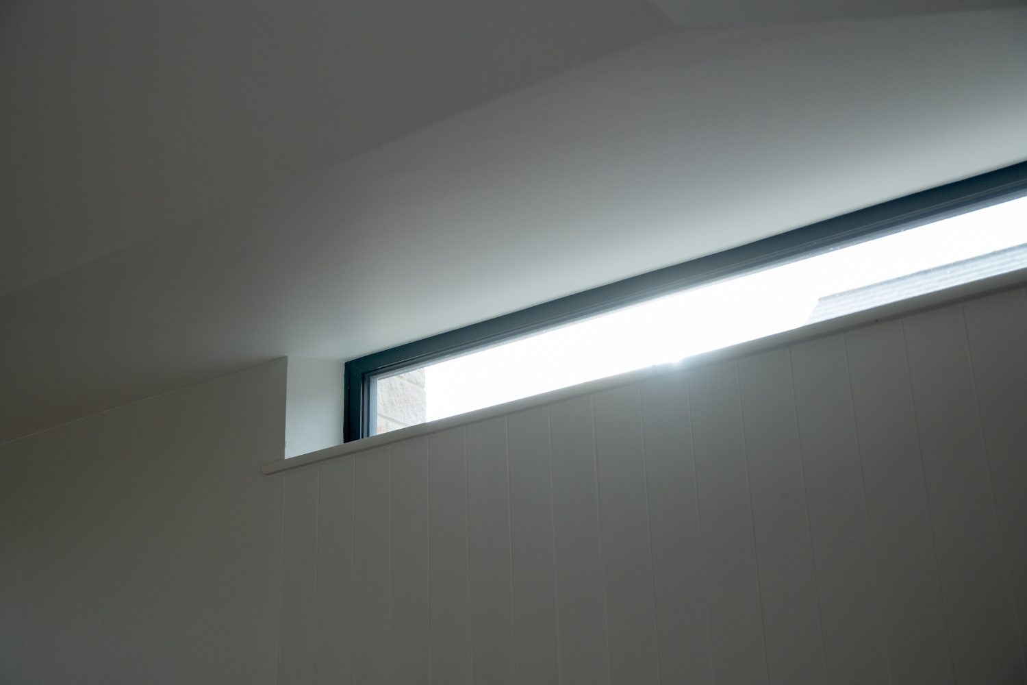 Thin horizontal window with cream panelled walls surrounding