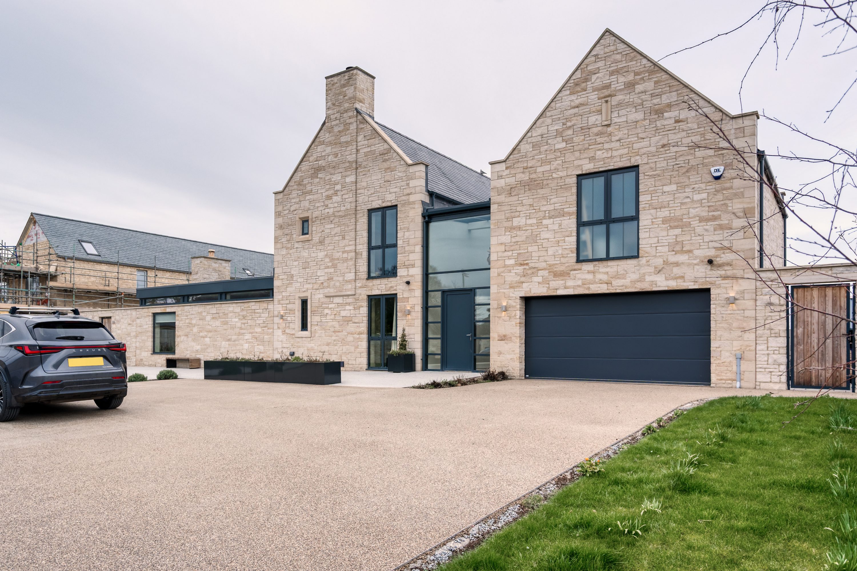 Exterior front of house with exposed stone walls, large black framed windows, black garage door and large driveway in front