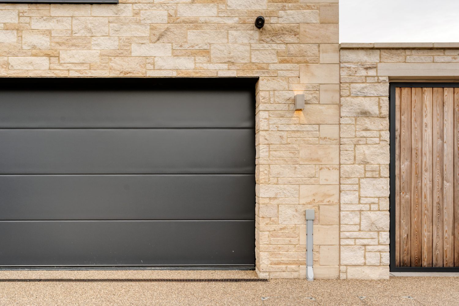 Exterior stone walls with black garage door on the left and wooden door on the right