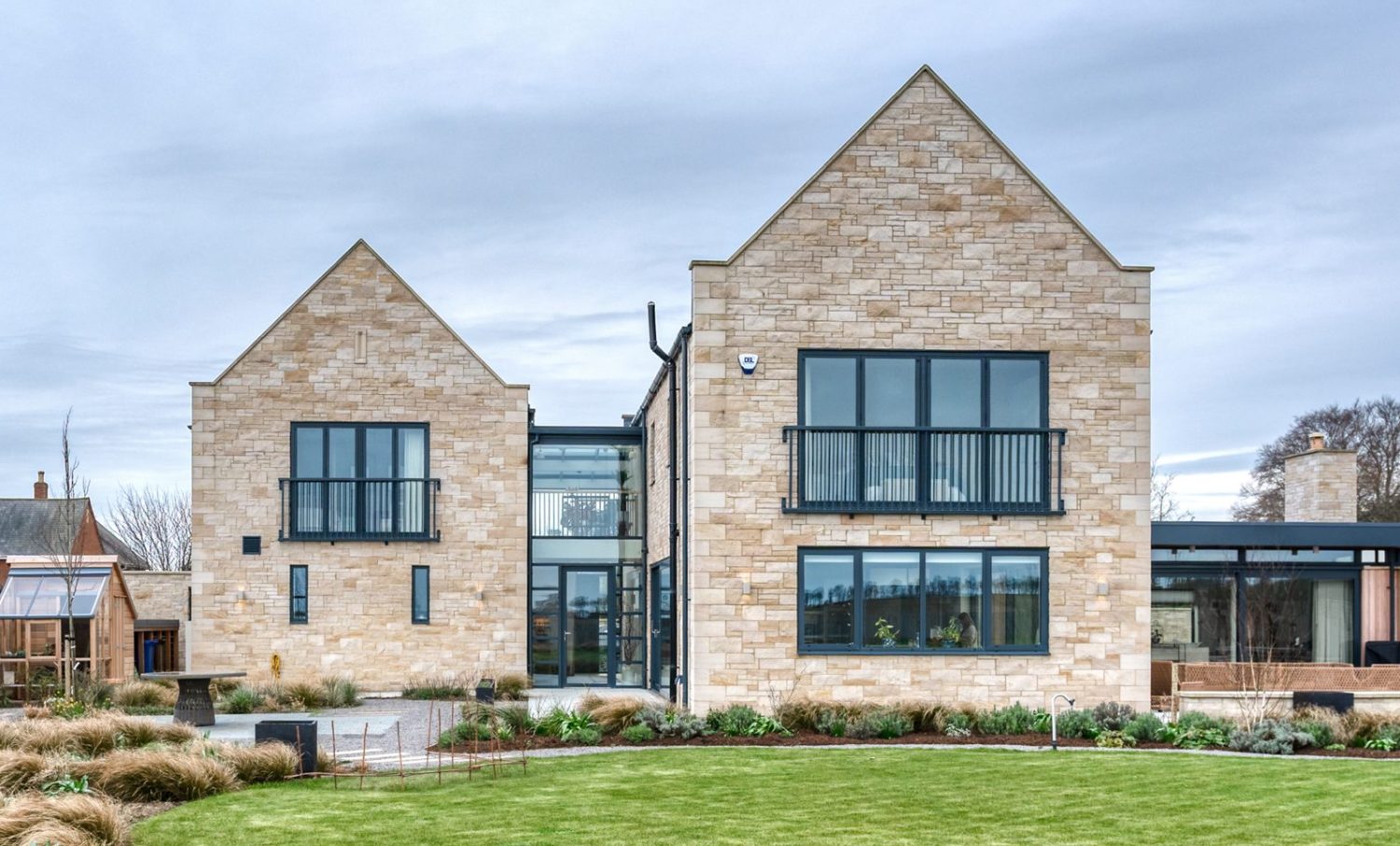 Garden behind house with exposed stone walls and large black framed windows