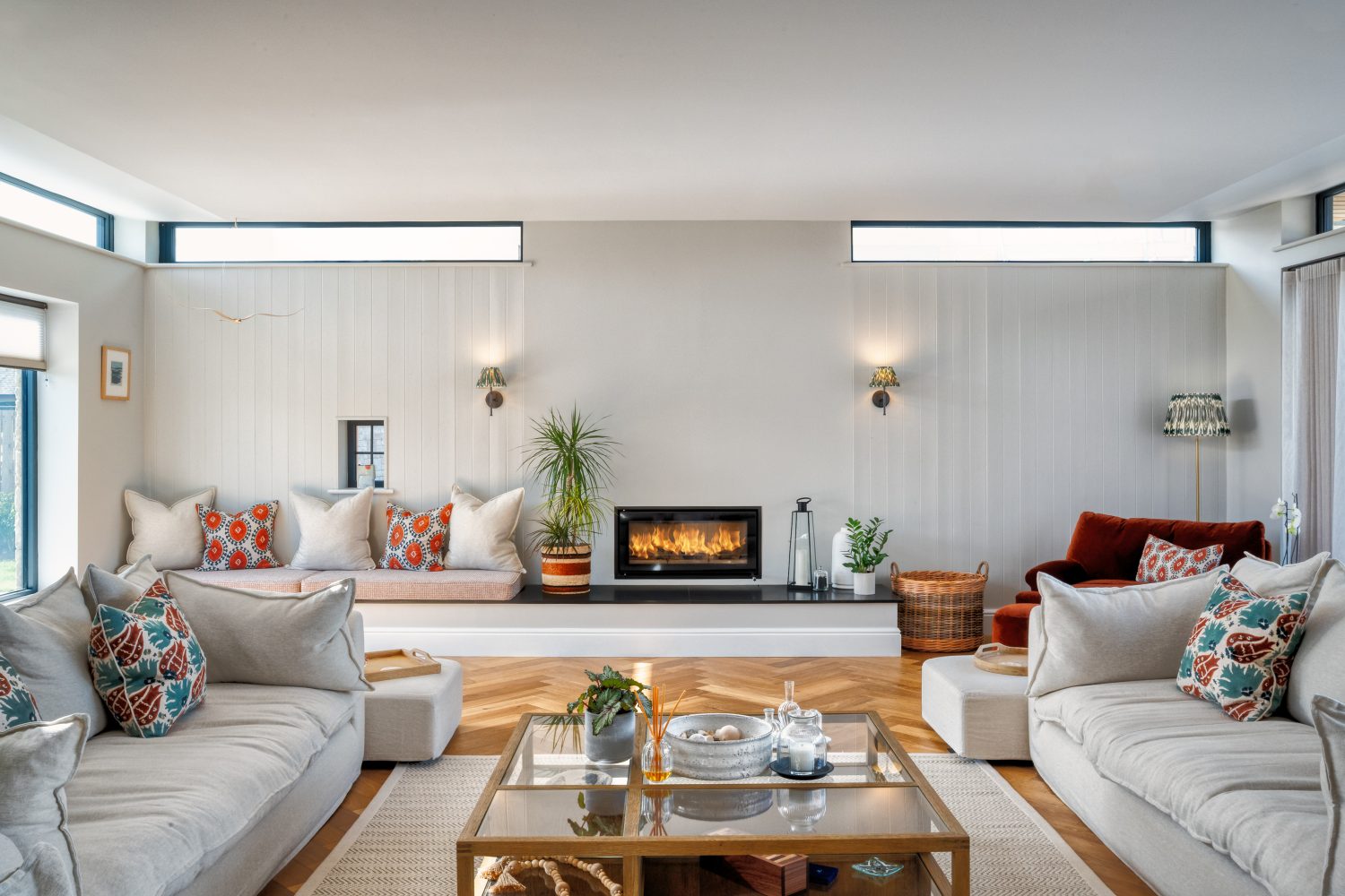 Living room with white sofas on either side, glass coffee table in centre, with fireplace and cushioned seating area to the back