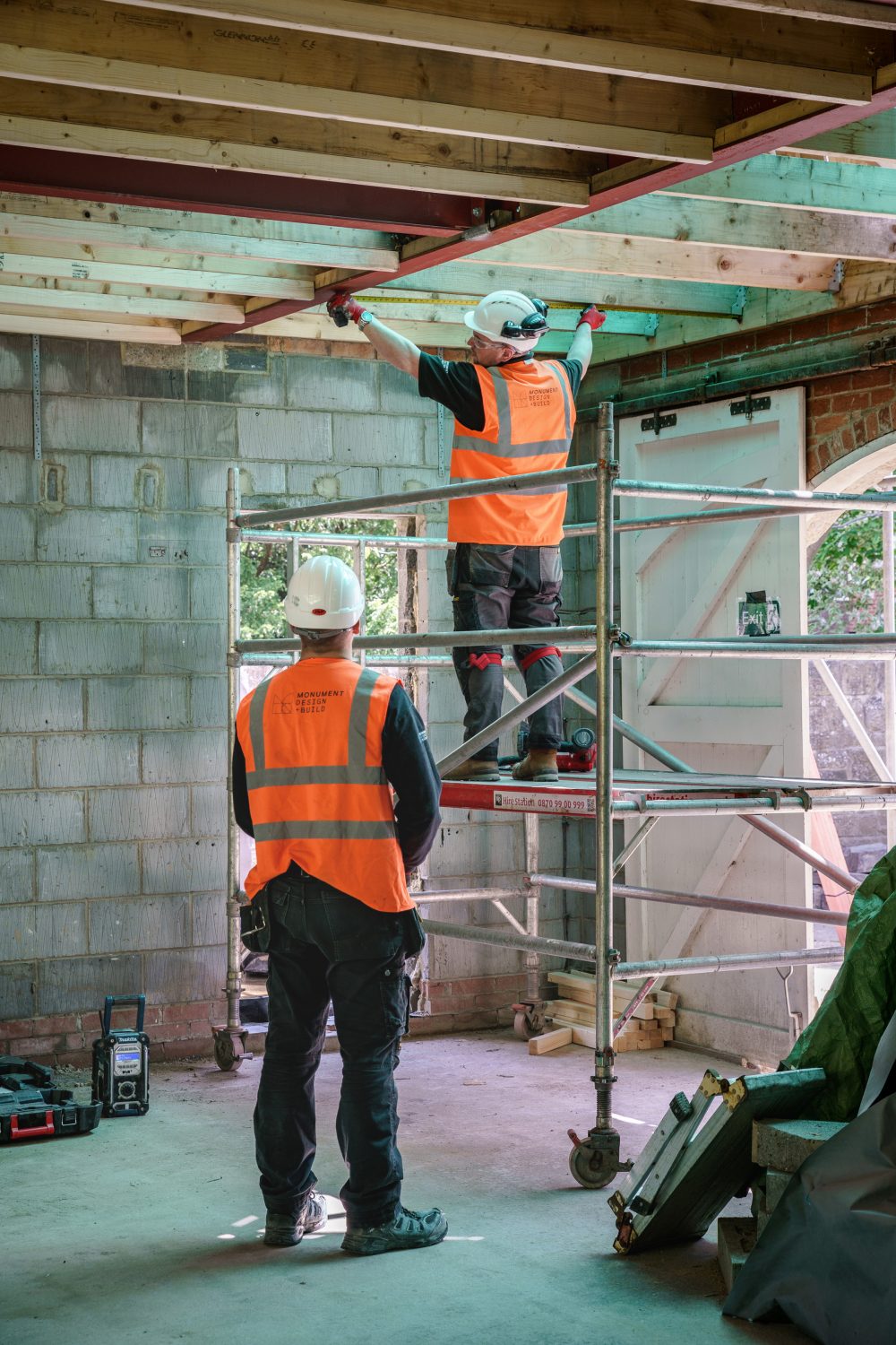 Two builders wearing orange hi vis working on a platform