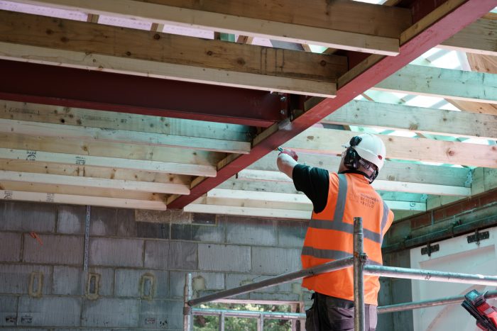 Builder in orange hi vis working on wooden beams above