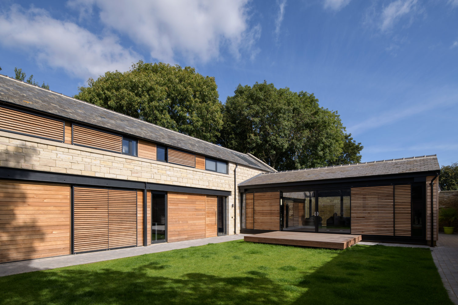 Stone built house with wooden panelling curving around a grass garden
