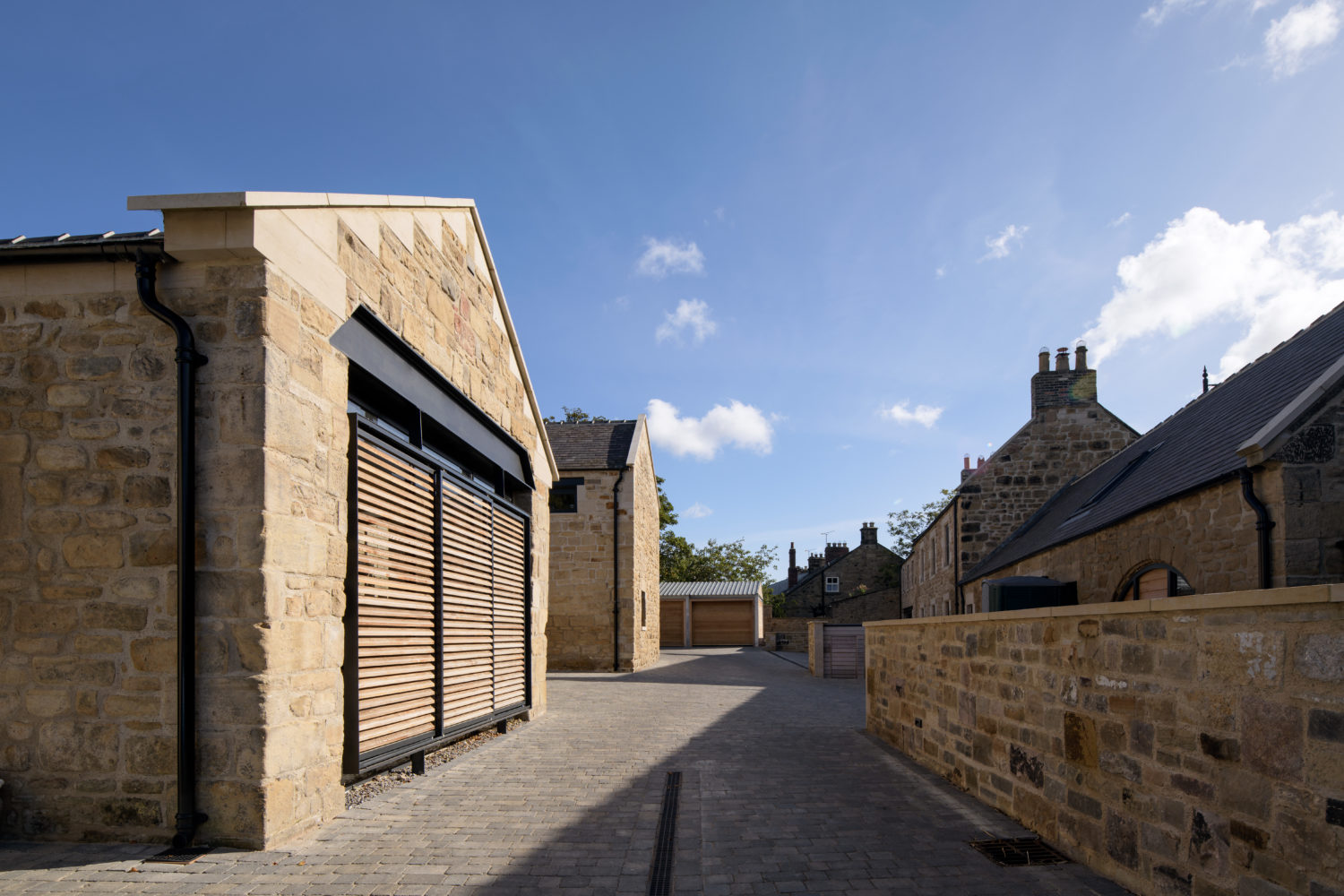 View down driveway with two stone built houses on the left and a stone wall on the right