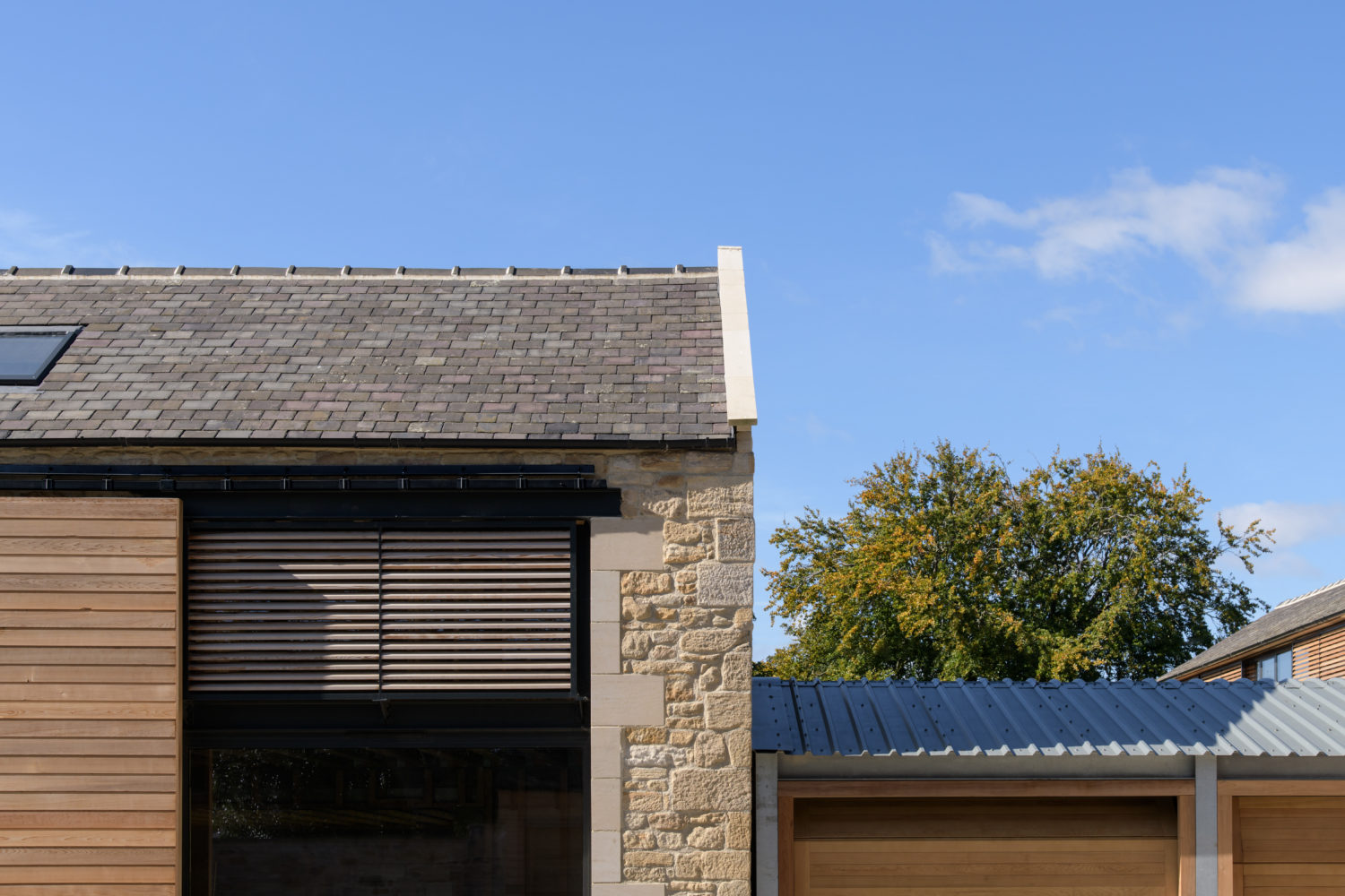 Corner of a stone built house with wooden shutters over a large window and blue sky behind