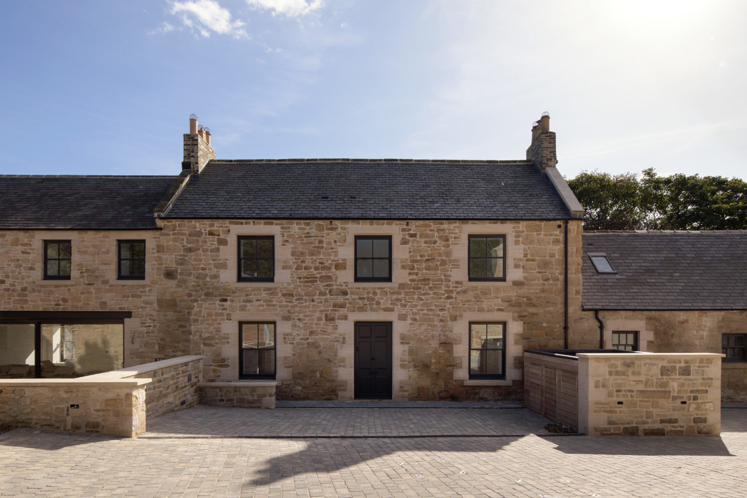 Front of a stone built house with stone walls on each side and blue skies above